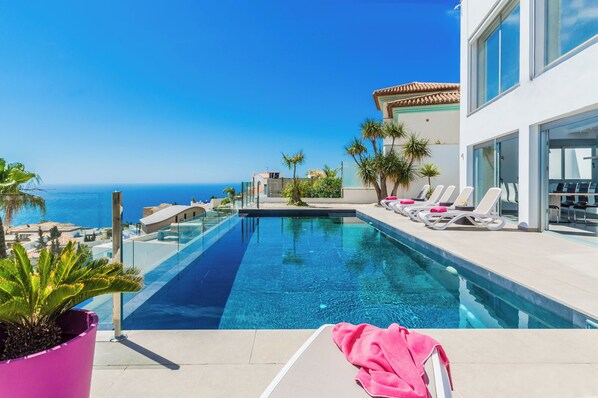 A modern infinity pool with clear blue water, surrounded by white lounge chairs and a pink towel. - Amazing modern villa with heated pool and breath taking view (Salobreña)