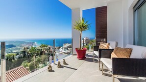 Un balcón con vista al mar, una planta en maceta y una zona de estar con cojines.