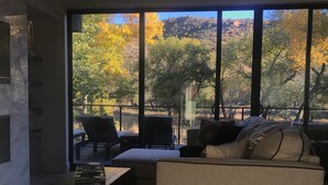 A modern living room with a large window offering a view of trees and hills. There is a sofa, a coffee table, and two chairs. - OBSERVATION POINT- 2 Miles from main entrance to ZNP New Barrel Sauna by river (Springdale)