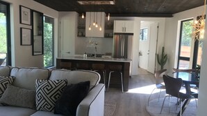 A modern living room with a sofa, a dining area with chairs, a kitchen with a central island, and a large window providing natural light. - OBSERVATION POINT- 2 Miles from main entrance to ZNP New Barrel Sauna by river (Springdale)