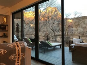 Ein geräumiger Balkon mit Blick auf eine felsige Landschaft und Bäume. Zwei Liegestühle und ein kleiner Tisch mit einem Stuhl sind vorhanden.