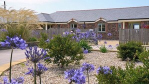 A cottage with a brick exterior, a wooden fence, and purple flowers in the garden. - Elm Cottage, Purpose Built Wheelchair Friendly Cottage (Truro)