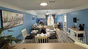 Un área de comedor con una mesa dispuesta para cuatro personas, un sofá, un televisor y una cafetera.