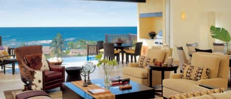 A modern living room with a view of the ocean, furnished with sofas, armchairs, and a coffee table.