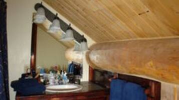 Un plafond en bois, une coiffeuse en bois avec un miroir, un lavabo et une serviette accrochée au mur.