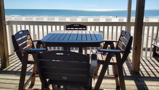Eine Holzterrasse mit Tisch und Stühlen mit Blick auf einen Strand.