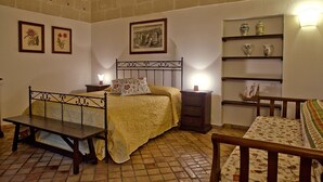 A bedroom with a bed, a bench, a bedside table, a nightstand, a chair, and shelves with decorative items.