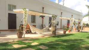 A white building with a covered outdoor seating area, including a hammock and potted plants.