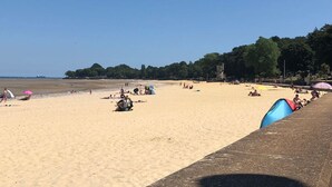 Una playa con gente relajándose y tomando el sol, un cielo despejado y un mar tranquilo.