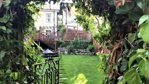 Un jardín bien cuidado con una valla de madera, una puerta metálica y un camino de piedra que lleva a una casa.