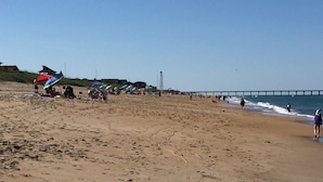 A sandy beach with footprints, a pier in the distance, and beach umbrellas.