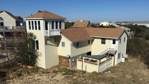 A two-story house with a balcony, a garage, and a sandy yard.