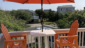 A wooden deck with two orange Adirondack chairs and a white table under a red umbrella.