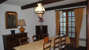 Ein Esszimmer mit Holztisch, Stühlen, einer Chandelierleuchtre, einem Spiegel und einem fenster mit Vorhängen.