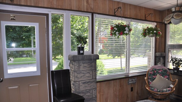 Una habitación con un pilar de piedra, una silla negra, un banco acolchado y una silla de mimbre con cojín floral.