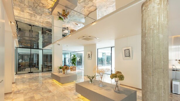 A modern lobby with marble flooring, glass walls, and a reception desk with plants. - Reno Hotel Bangkok (Bangkok)