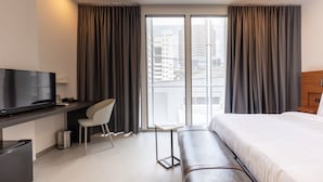 A modern hotel room with a large bed, a desk with a TV, a chair, and a view of the city through large windows. - Reno Hotel Bangkok (Bangkok)