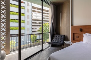 A hotel room with a bed, a chair, a small table, and a view of a building with greenery outside. - Reno Hotel Bangkok (Bangkok)