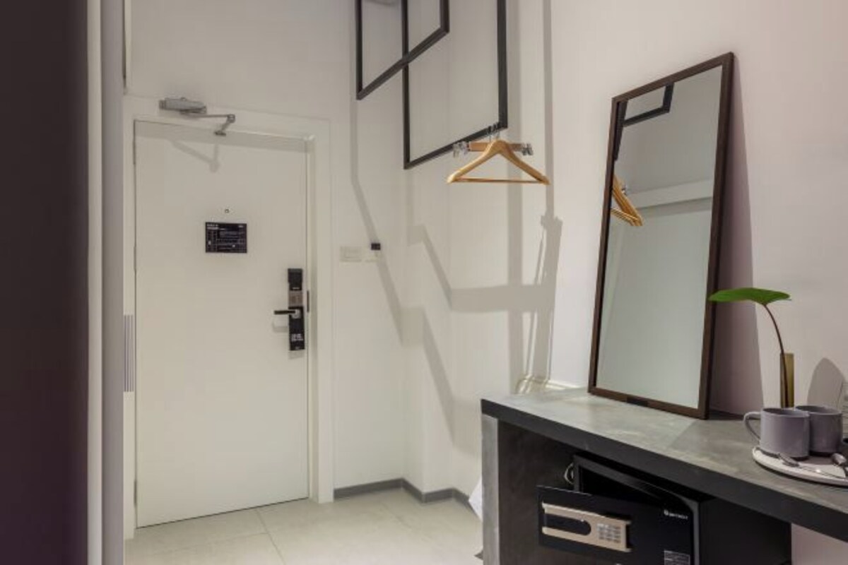 A modern hotel room with a white door, a black-framed mirror, a black console table, and a small plant.