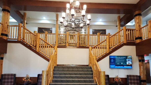 A grand staircase with wooden railings and a chandelier, leading to a second floor.