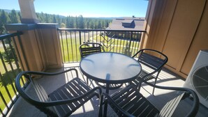 A balcony with a table and chairs, overlooking a green landscape and distant mountains.