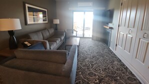 A living room with a sofa, armchairs, a coffee table, a lamp, a ceiling fan, a TV, and a patterned carpet.