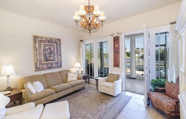 A living room with a beige sofa, a white armchair, a patterned rug, a chandelier, and a large painting. - Steps to Beach - Private LakeFront House-Private Pool-Laguna / Panama City Beach (Panama City Beach)