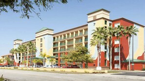 A multi-story hotel with a central courtyard, palm trees, and a parking lot.