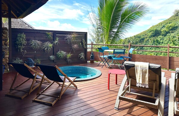 A wooden deck with a hot tub, lounge chairs, and potted plants.