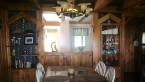 Une salle à manger en bois avec une grande table, des chaises et des étagères remplies de livres et d’ustensiles de cuisine.