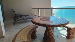 Un balcon doté d’un sol carrelé, une table ronde ornée de motifs en mosaïque et deux fauteuils.