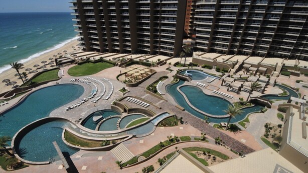 Un complexe hôtelier doté de plusieurs piscines, d’une plage et d’un grand bâtiment en arrière-plan.
