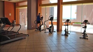 Une salle de sport équipée de tapis de course, de vélos elliptiques et où une personne utilise un vélo elliptique.