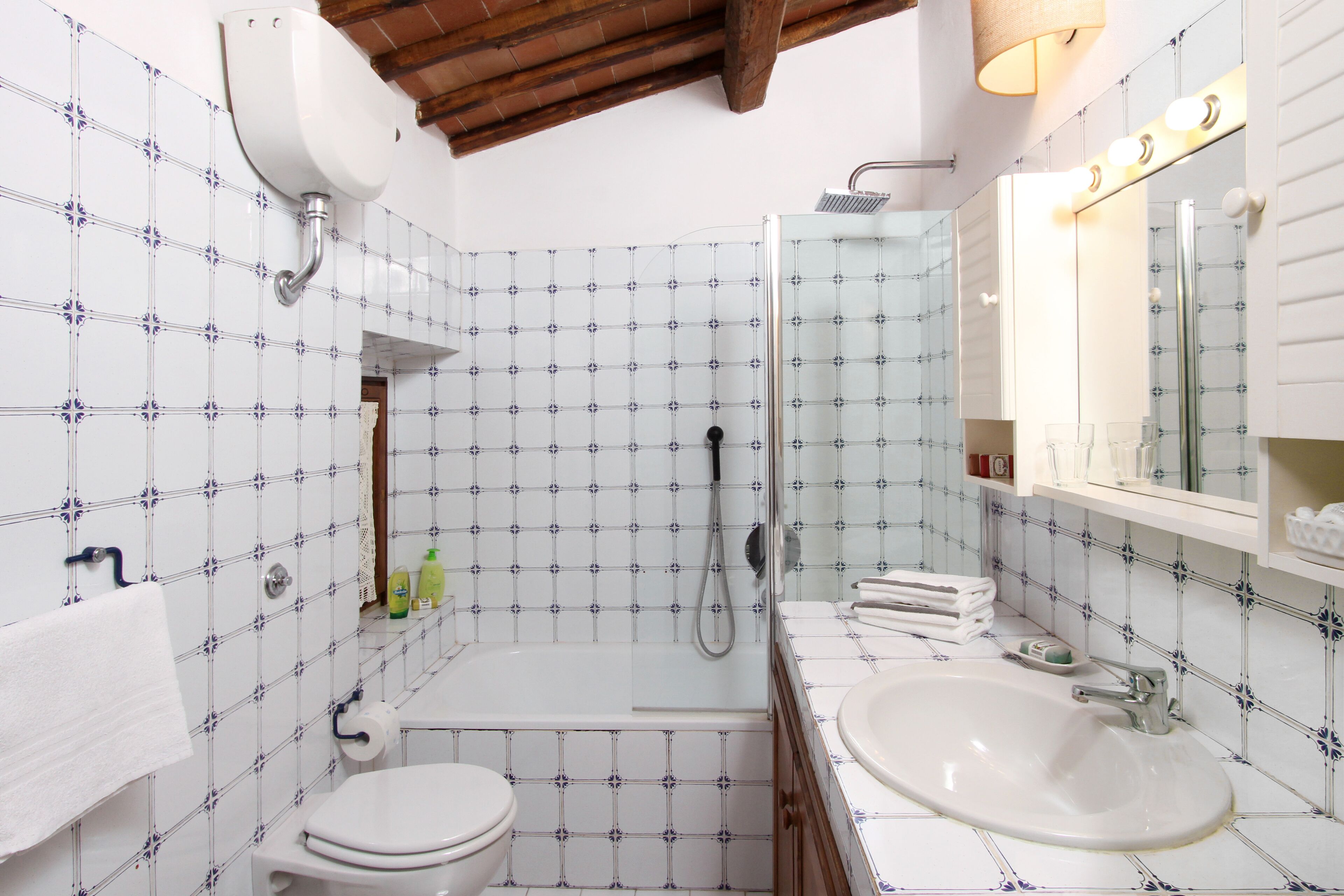Une salle de bain équipée d’une baignoire, de toilettes et d’un lavabo, avec des carreaux décoratifs et des poutres en bois.