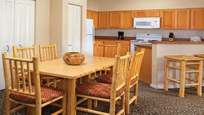 A compact kitchen with wooden cabinets, a microwave, a stove, and a dining table with chairs.