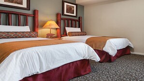 A hotel room with two beds, each with a white comforter and a brown accent. There is a wooden headboard, a lamp, and a framed picture on the wall.