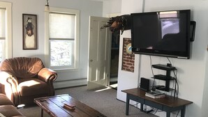 A living room with a brown leather couch, a wooden coffee table, a television mounted on the wall, and a fireplace. - Brookside House-Large, charming Historic Home. Pet Friendly! (Greenwood)