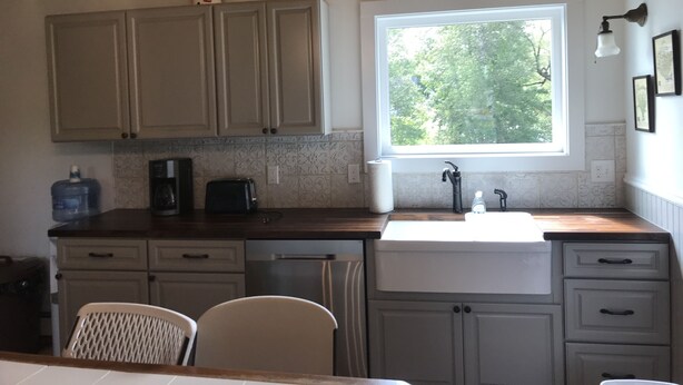 A kitchen with wooden cabinets, a window with a view of trees, a sink, and a toaster. - Brookside House-Large, charming Historic Home. Pet Friendly! (Greenwood)