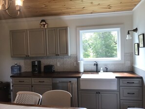 Una cocina con armarios de madera, una ventana con vistas a árboles, un lavabo y un tostador.