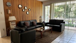 Een moderne woonkamer met een zwarte leren bank, een bijzettafeltje en een houten wand met klokken en spiegels.
