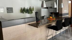 Een moderne keuken met een centraal eiland, roestvrijstalen apparatuur en hangende wijnflessen.
