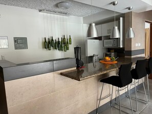 A modern kitchen with a central island, stainless steel appliances, and hanging wine bottles.