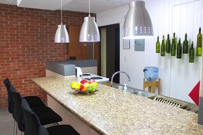 Una cocina con encimeras de granito, electrodomésticos de acero inoxidable, lámparas colgantes y un dispensador de agua.