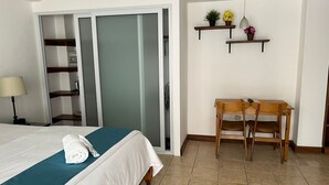 Een hotelkamer met een bed, een bureau met twee stoelen, een lamp en een plank met planten.
