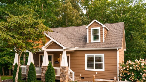 A two-story house with a brown exterior, white trim, a stone pillar, and a porch with a railing.