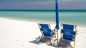 Two beach chairs with a blue umbrella on a sandy beach. - Summerwind West #202 Oceanfront Condo - Free Beach Chairs & Umbrella. (Navarre Beach)