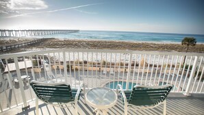 A balcony with a glass table and two chairs, overlooking a beach and a pier. - Summerwind West #202 Oceanfront Condo - Free Beach Chairs & Umbrella. (Navarre Beach)