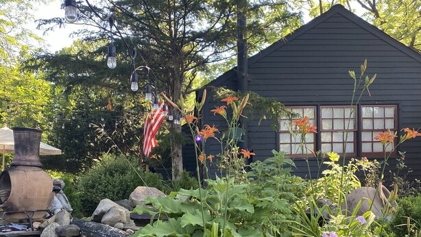 A garden with a variety of plants, a stone wall, and a house with windows. - Cozy designer Cottage on private historic estate-near NYC-Oasis in Metropolis (West Caldwell)