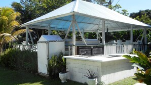 A covered outdoor area with a grill and seating, surrounded by greenery. - Chippewa Village Pool Apt  (Negril)