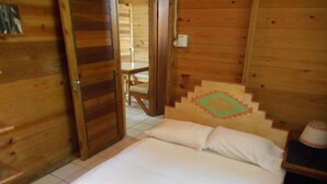 A wooden cabin room with a bed, a chair, and a staircase with a decorative headboard. - Chippewa Village Pool Apt  (Negril)